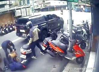 A pit bull jumps out of a car and attacks a man on a scooter